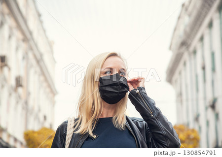 Woman in the background of the city wants to remove a black protective face mask 130854791