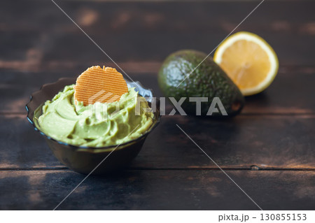 Traditional latinamerican mexican sauce guacamole in bowl with cracker, avocado and lemon on dark background 130855153
