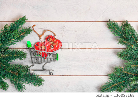 Christmas shopping - small shopping cart with gifts and fir branches on wooden background 130855169