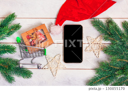 Christmas shopping online - small shopping cart with gifts, smartphone and fir branches on wooden background 130855170