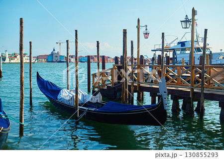 Venetian gondola moored at wooden pier with city waterfront in background 130855293