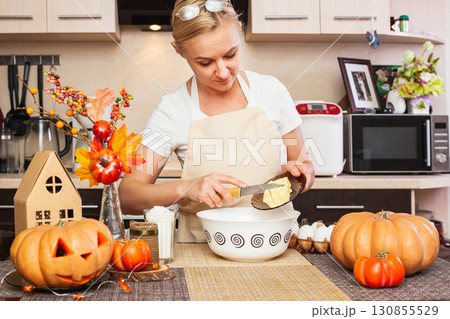 A woman puts butter in the cookie dough for Halloween in the kitchen with autumn decor. 130855529