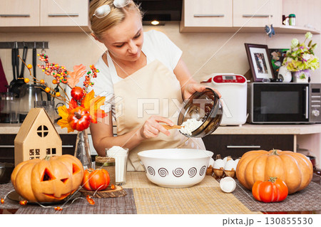 A woman puts cottage cheese in cookie dough for Halloween in the kitchen with autumn decor. 130855530