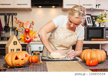 A woman kneads cookie dough for Halloween in the kitchen with autumn decor. A woman kneads cookie dough for Halloween in the kitchen with autumn decor. 130855534