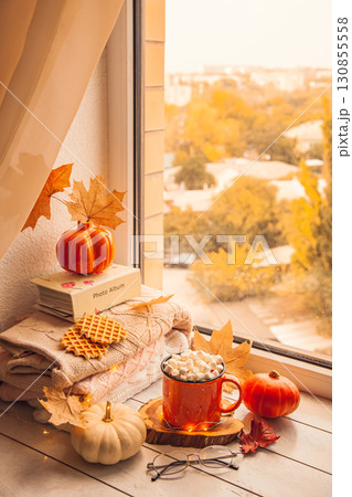 Cozy autumn still life on the windowsill: warm wool sweaters, pumpkins, maple leaves and a Cup of cocoa with marshmallows Cozy autumn still life on the windowsill: warm wool sweaters, pumpkins, maple leaves and a Cup of cocoa with marshmallows 130855558