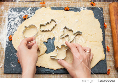 Making cookies for Halloween. A woman cuts out cookies from the dough in the form of pumpkin, cat, Ghost and bat Making cookies for Halloween. A woman cuts out cookies from the dough in the form of pumpkin, cat, Ghost and bat 130855598