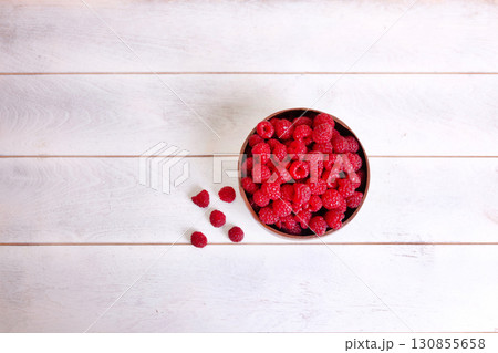 Raspberries in coconut shell bowl on white wooden background 130855658