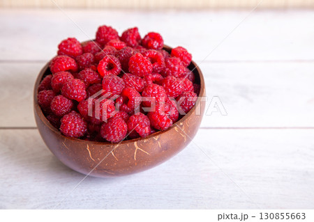 Raspberries in a coconut shell bowl on a white wooden background Raspberries in a coconut shell bowl on a white wooden background 130855663