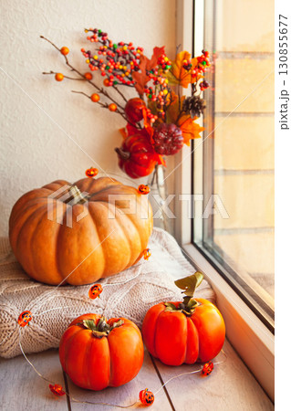 Cozy autumn still life on the windowsill: pumpkin, warm wool sweaters, maple leaves and persimmon Cozy autumn still life on the windowsill: pumpkin, warm wool sweaters, maple leaves and persimmon 130855677
