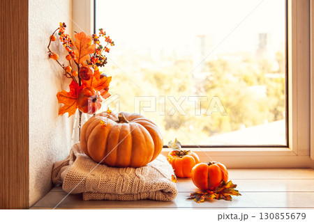 Cozy autumn still life on the windowsill with copy space: pumpkin, warm wool sweaters, maple leaves and persimmon. 130855679