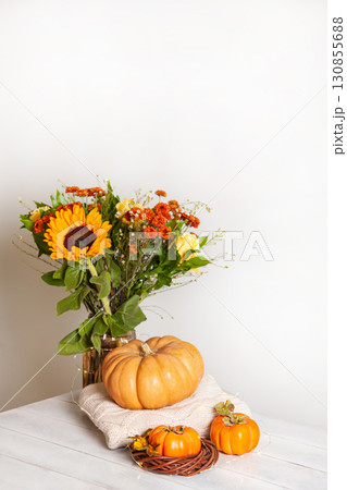 Cozy autumn still life on wooden background with bouquet of sunflowers, pumpkin, warm wool sweaters and persimmon 130855688