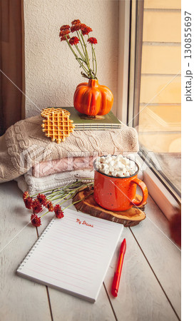 Cozy autumn still life on the windowsill with Notepad for notes: warm wool sweaters, pumpkins, maple leaves and a Cup of cocoa with marshmallows and waffles 130855697