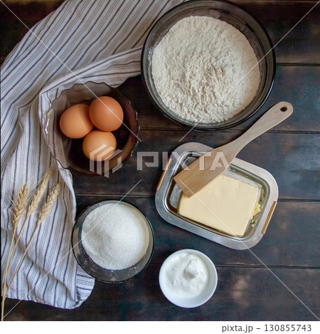 Baking ingredients for shortcrust pastry: butter, flour, eggs, sour cream, a towel on a wooden background. Flatley top view 130855743