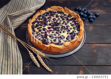 Rustic shortbread pie with blueberries in sour cream filling on a wooden background with kitchen towel and wheat ears 130855751