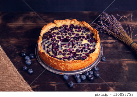 Rustic shortbread pie with blueberries in sour cream filling on a wooden background and a bouquet of dried lavender. 130855758