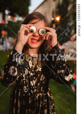 Girl wearing halloween costume holding fake eyeballs in front of her eyes 130856163