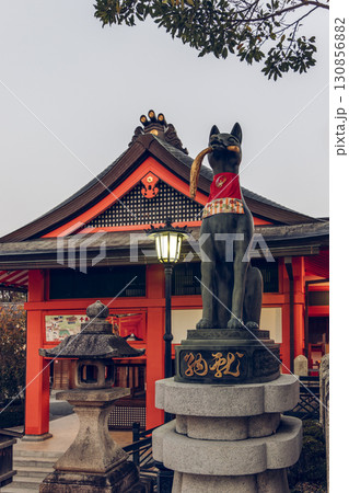Traditional fox statue at Fushimi Inari Taisha Kyoto near stone lantern and gate in morning sunlight 130856882