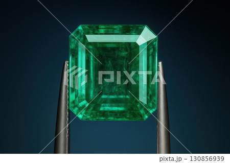 Emerald Gemstone in Tweezers against Deep Blue Background 130856939