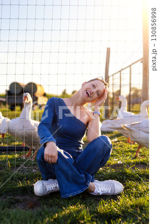 Portrait young adult happy smiling woman wear jeans denim jumpsuit enjoy having fun countryside farm animal geese flock warm sunset light. Female person rural country village farmyard bird poultry Portrait young adult happy smiling woman wear jeans denim jumpsuit enjoy having fun countryside farm animal geese flock warm sunset light. Female person rural country village farmyard bird poultry 130856998
