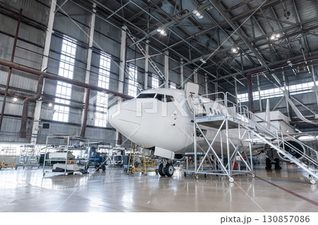 White passenger plane in the airplane hangar. Aircraft under maintenance. Checking mechanical systems for flight operations 130857086