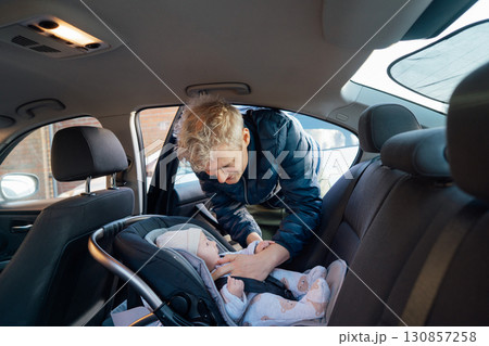 Father putting baby in safety car seat happy family vacation road trip lifestyle child care transportation rear-facing. Caring parent secures baby by fastening with seat belt. Selective focus. 130857258