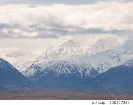 Snow capped mountain range under cloudy sky. View from telephoto lens of distant high mountains covered with snow at the top. Mountain view in Kurai steppe, Altai Republic 130857522