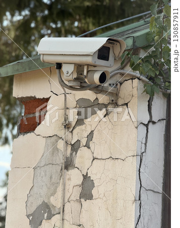 Security camera mounted on cracked building wall showing urban decay and infrastructure Security camera mounted on cracked building wall showing urban decay and infrastructure 130857911
