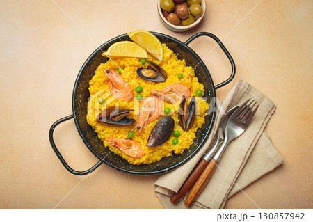 Spanish seafood Paella with shrimps, mussels, peas and lemon in a pan on light beige background top view 130857942