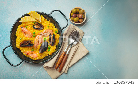 Spanish seafood Paella with shrimps, mussels, peas and lemon in a pan on light blue background top view. Mediterranean meal, space for text 130857945