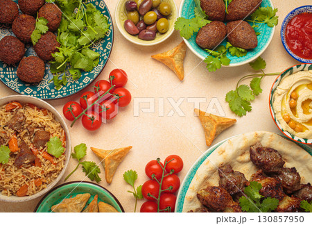 Top view of a vibrant table filled with lebanese dishes and mezze, featuring meat kebabs, falafel, kibbeh, hummus, sambousek, rice, olives. Middle eastern or Arab dishes, space for text Top view of a vibrant table filled with lebanese dishes and mezze, featuring meat kebabs, falafel, kibbeh, hummus, sambousek, rice, olives. Middle eastern or Arab dishes, space for text 130857950