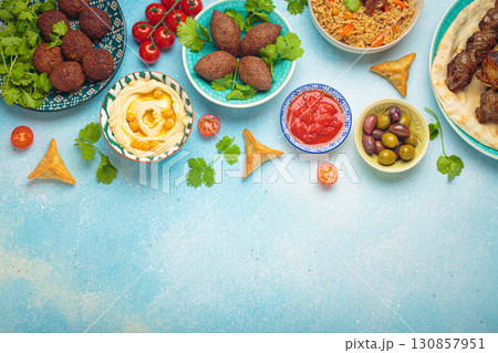 Top view of a vibrant table filled with lebanese dishes and mezze, featuring meat kebabs, falafel, kibbeh, hummus, sambousek, rice, olives. Middle eastern or Arab dishes, space for text Top view of a vibrant table filled with lebanese dishes and mezze, featuring meat kebabs, falafel, kibbeh, hummus, sambousek, rice, olives. Middle eastern or Arab dishes, space for text 130857951
