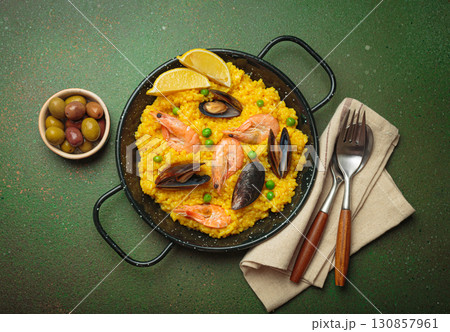 Spanish seafood Paella with shrimps, mussels, peas and lemon in a pan on green rustic background top view 130857961