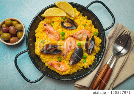 Spanish seafood Paella with shrimps, mussels, peas and lemon in a pan on light blue background top view. Mediterranean meal 130857971