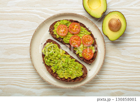 Healthy avocado toast with green peas and cherry tomatoes on whole rye bread top view on white wooden background 130858001