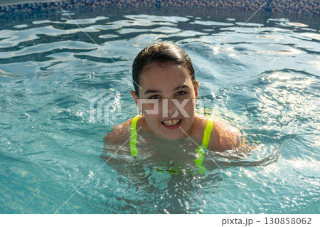 Smiling hispanic female child swimming in pool with bright green swimsuit 130858062