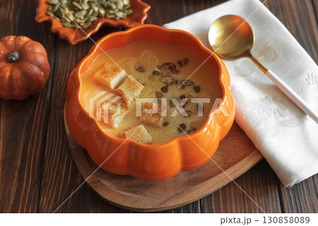 Creamy pumpkin soup with croutons and seeds, served in a pumpkin-shaped bowl on dark wooden table. Top view Creamy pumpkin soup with croutons and seeds, served in a pumpkin-shaped bowl on dark wooden table. Top view 130858089