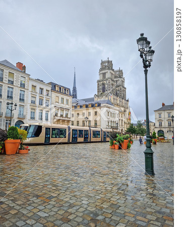 Orleans city center and a tram moving across the wet cobblestone square, with the ornate towers of the Sainte-Croix cathedral visible in background Orleans city center and a tram moving across the wet cobblestone square, with the ornate towers of the Sainte-Croix cathedral visible in background 130858197