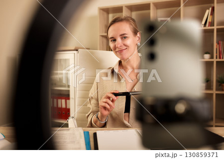 Professional woman smiling while recording video in modern office setting 130859371