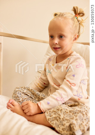 Young girl sitting on a bed with patterned pajamas 130859373