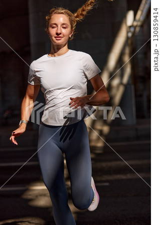 Young woman jogging outdoors in sunlight with energetic and focused expression 130859414