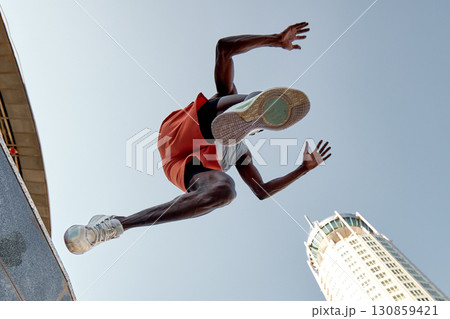 Low angle view of athlete jumping amidst urban skyscrapers on a bright day 130859421