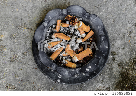 Background surface of ashtray with smoked cigarettes placed on concrete ground 130859852