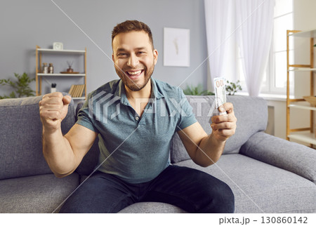 Portrait of a satisfied young bearded man holding dollars and doing winner gesture. 130860142