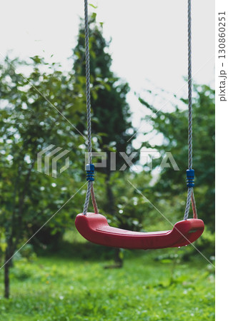 Lonely red hanging swings in green garden background Lonely red hanging swings in green garden background 130860251