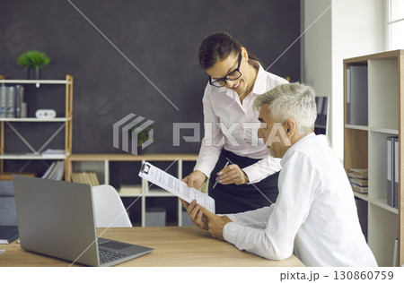 Senior businessman reads a document brought to him by his secretary before signing it. Senior businessman reads a document brought to him by his secretary before signing it. 130860759
