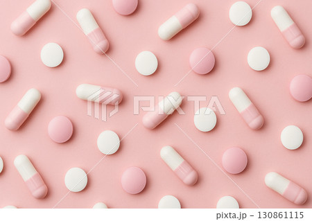 Assorted white and pink capsules and round pills scattered on pastel pink background, creating soft and modern pharmaceutical concept with clean and organized pattern 130861115