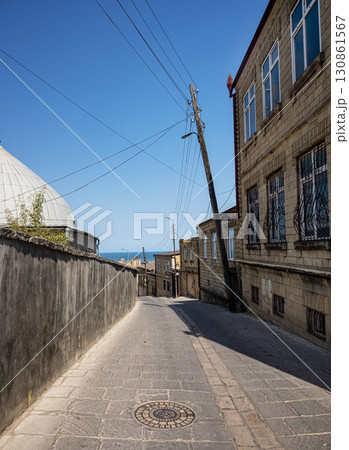 A narrow cobbled street with old stone buildings, power poles and the sea in the distance 130861567
