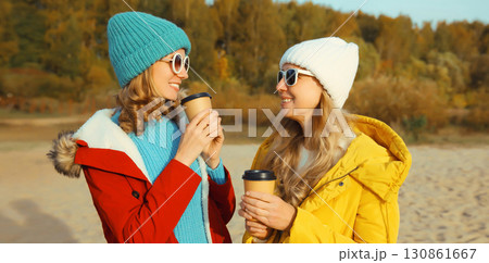 Happy two women friends talking on sunny beach, stylish girlfriends smiles together on sea coast 130861667
