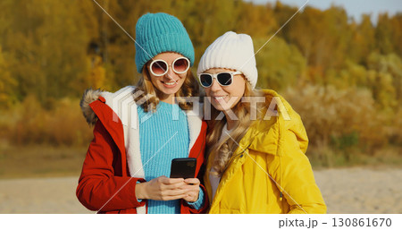 Happy young women friends with smartphone together on beach, smiling girlfriends using phone on sea 130861670