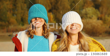 Happy two women friends having fun in knitted winter hat over her face, funny girlfriends together Happy two women friends having fun in knitted winter hat over her face, funny girlfriends together 130861689